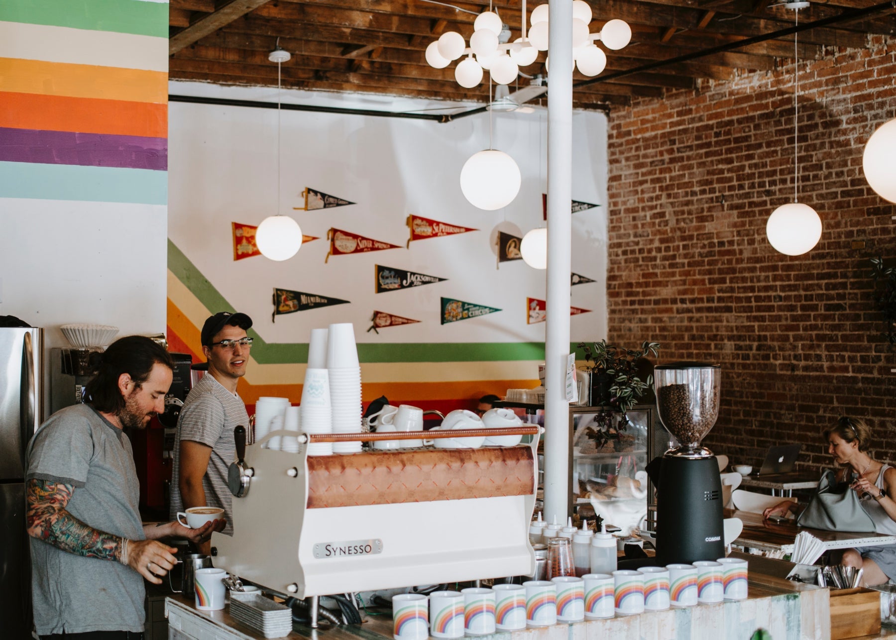 Baristas working in a cozy café with rainbow stripes and vintage pennants on the wall.