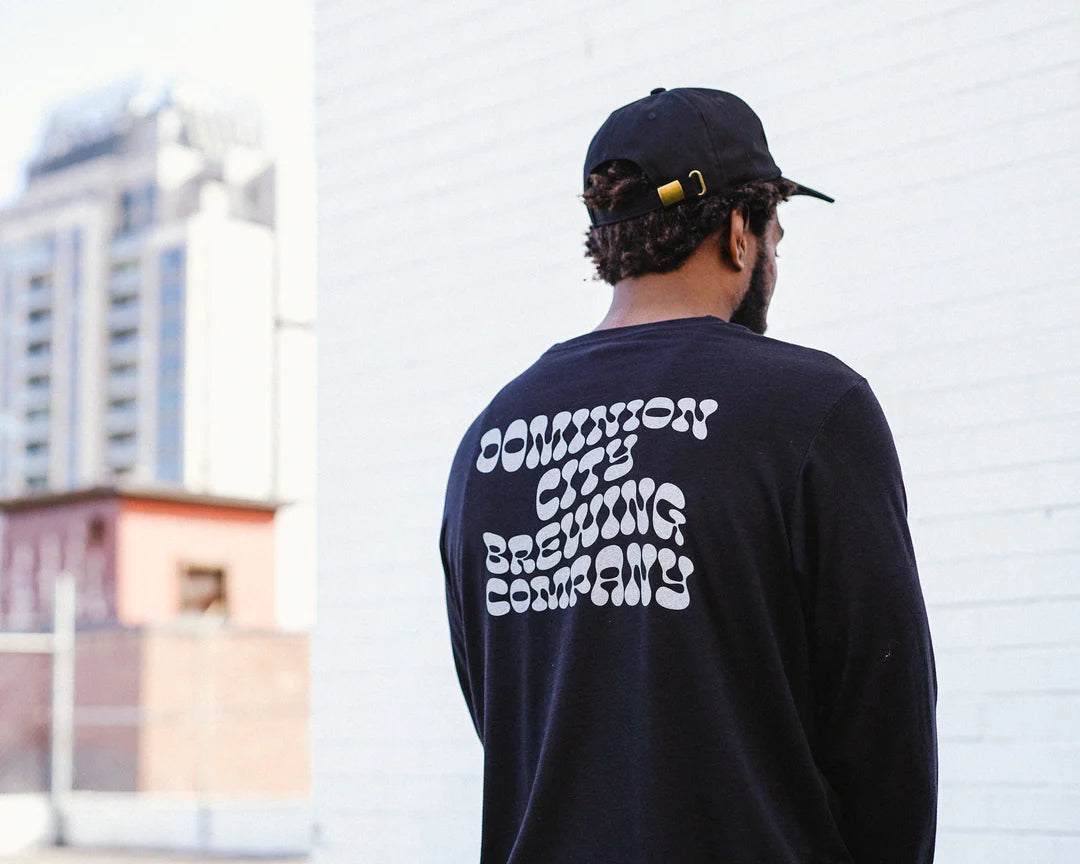 Person wearing a black long-sleeve shirt with Dominion City Brewing Company text on the back.
