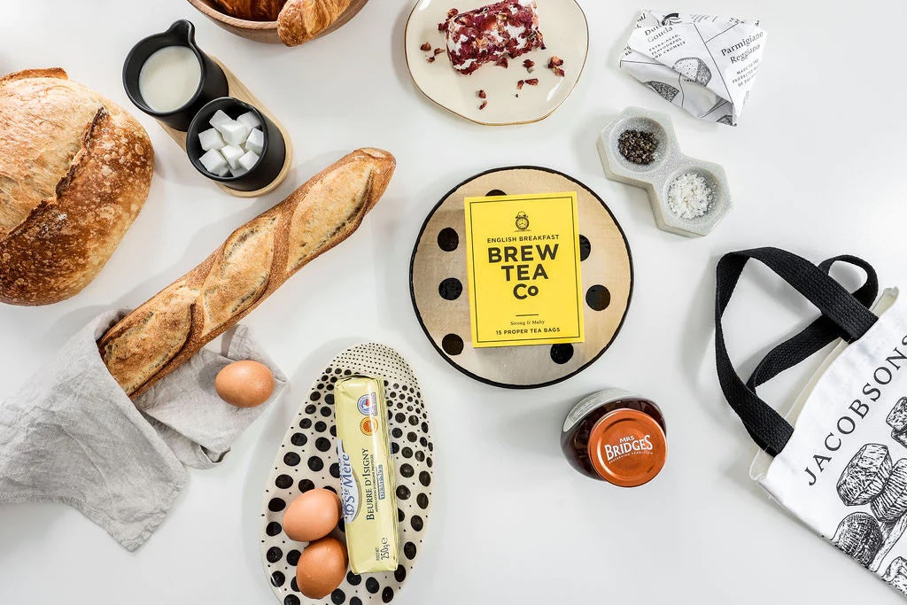 Overhead view of bread, eggs, tea, jam, and cheese displayed on a white table.