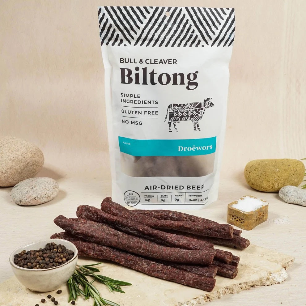 A Bull & Cleaver package next to air-dried beef sticks displayed with herbs, salt, and pepper.