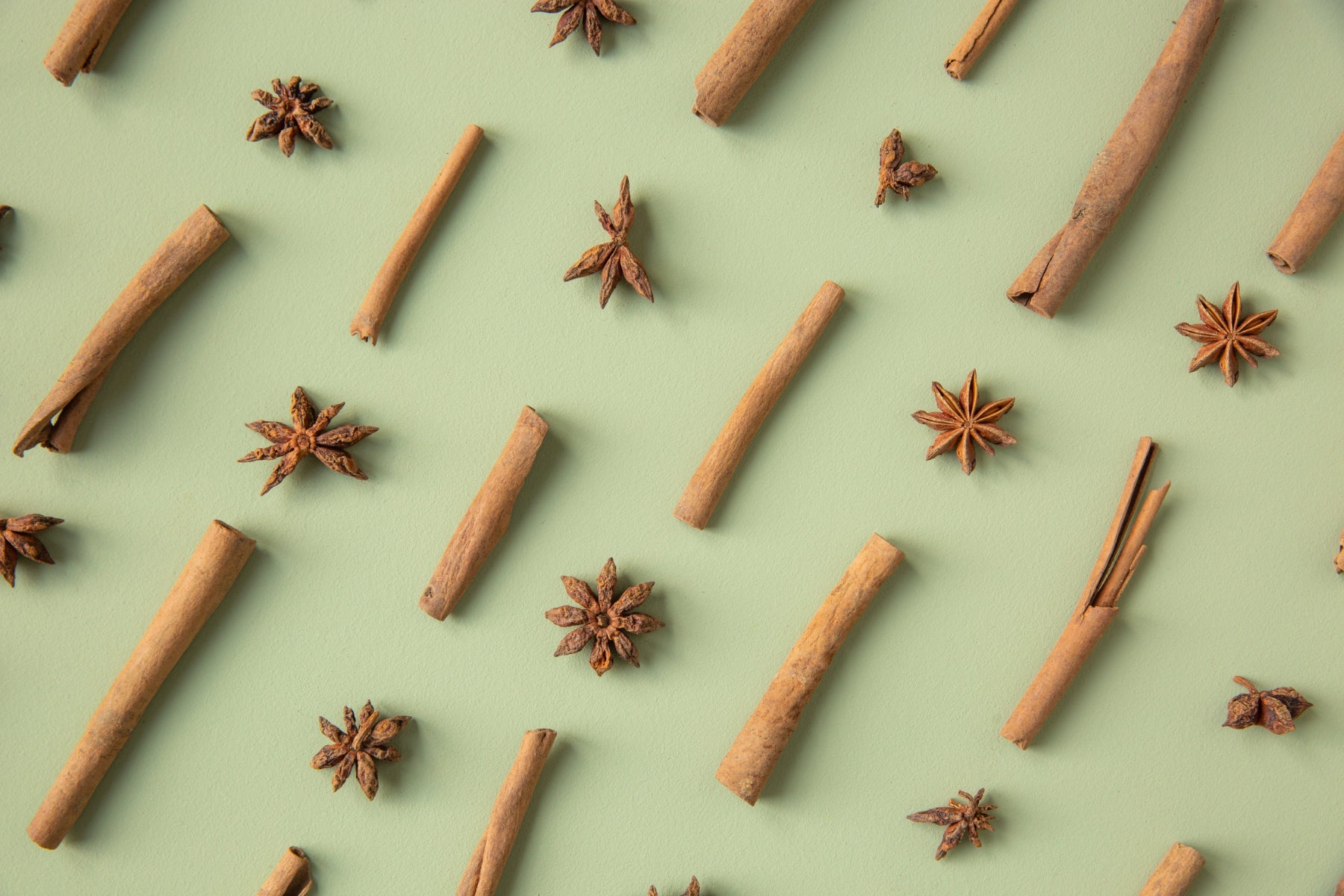 Star anise and cinnamon arranged in a pattern on a mint green background.