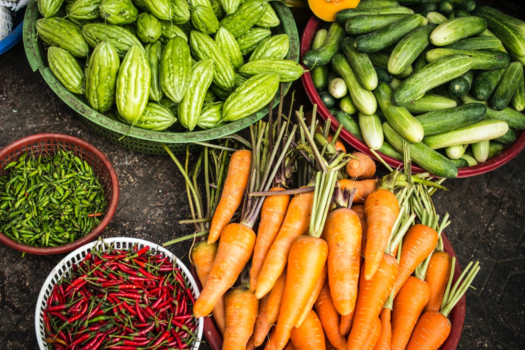 Baskets filled with carrots, cucumbers, bitter melons, and red and green chili peppers.