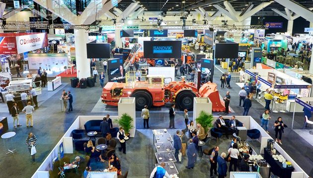 A photograph of a crowd of business people gathered around a speaker at a trade show.