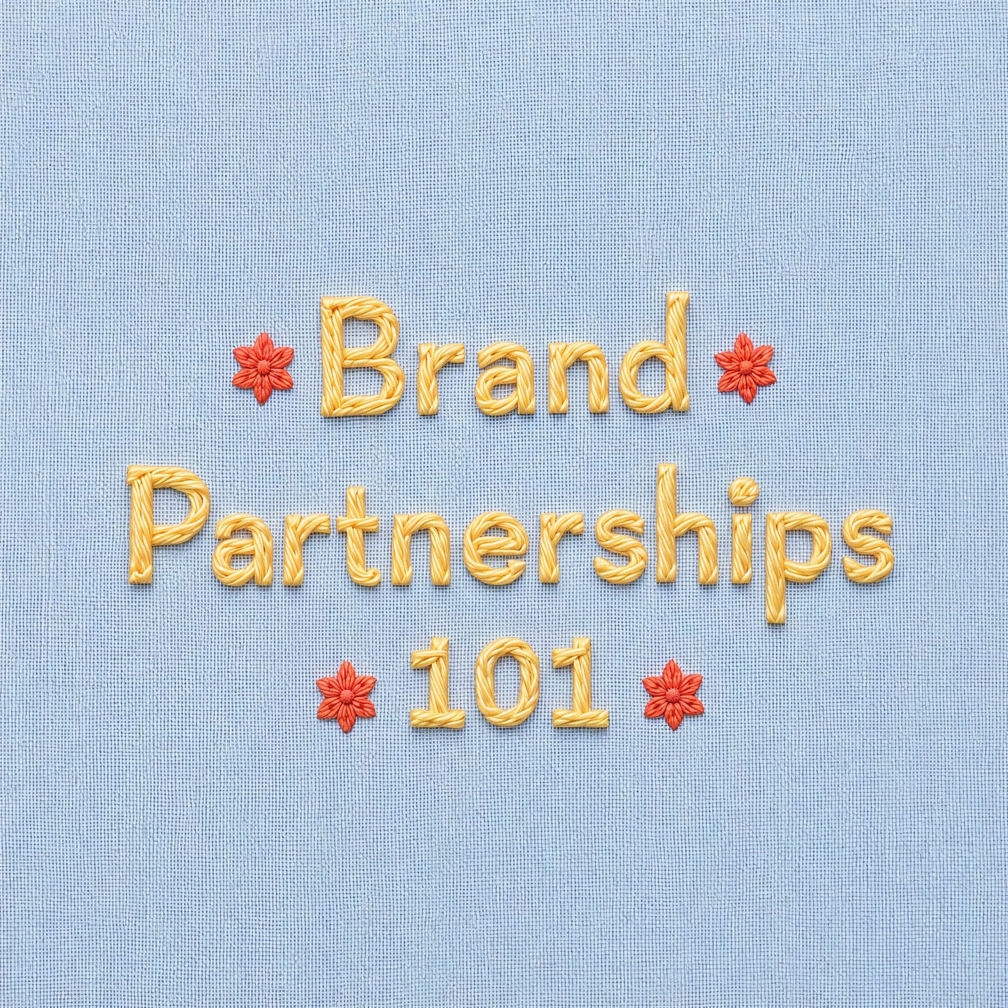 Lucid Origin AI image generator artwork featuring embroidered Brand Partnerships 101 text in gold thread with red floral accents on light blue fabric.